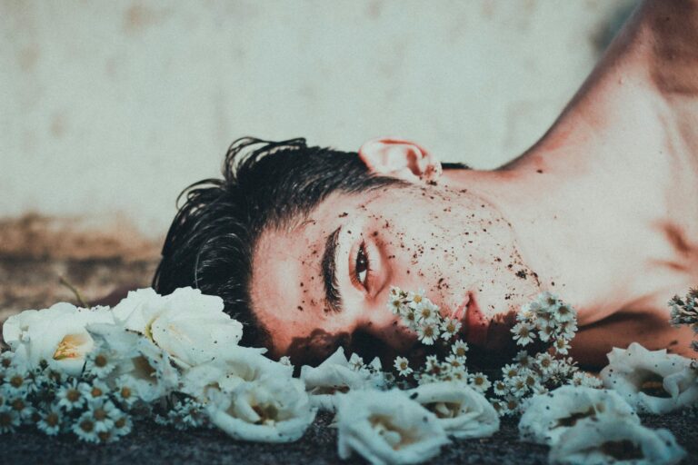 An ethereal portrait of a young adult male lying among flowers, conveying themes of vulnerability and mental health.